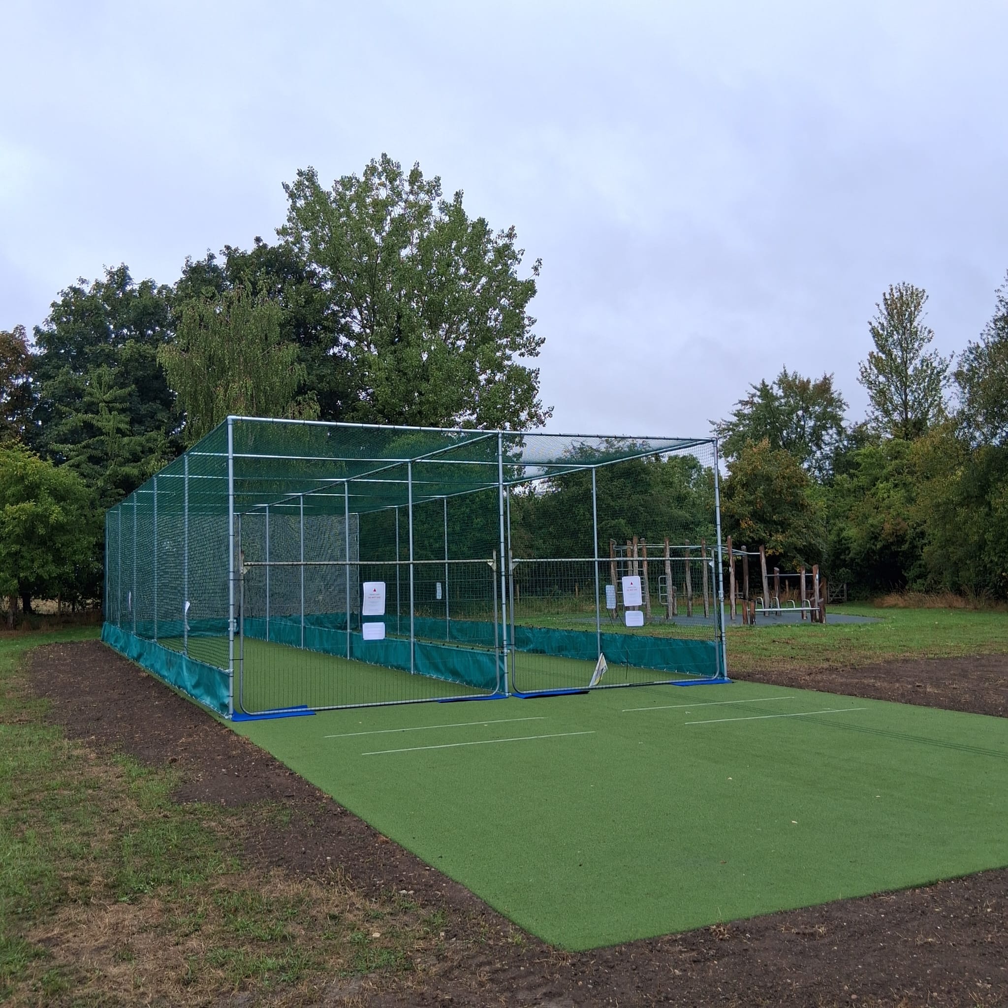Cricket Practice Nets in the foreground with trees and a pale blue sky.